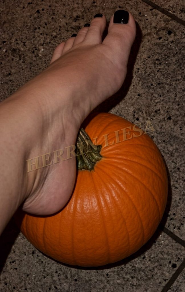 Ein Fuß mit schwarz lackierten Nägeln liegt auf einem orangefarbenen Kürbis.